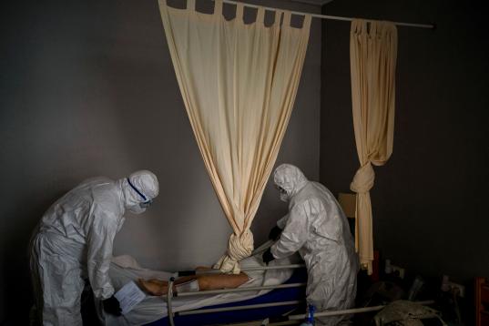 Con trajes de protección para evitar infecciones, dos trabajadores de una funeraria preparan el cuerpo de un anciano fallecido por COVID-19 antes de retirarlo de un centro de mayores, en Barcelona, el 13 de noviembre de 2020. 