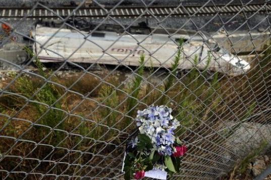 Un ramo de flores recuerda a las víctimas con la destrozada locomotora del tren al fondo