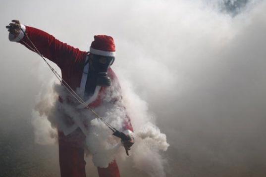 Un palestino, vestido de Papá Noel, utiliza un tirachinas para devolver el gas lacrimógeno lanzado por las tropas israelíes durante los enfrentamientos en una manifestación en contra de los asentamientos judíos en Bilin, Ramallah, Palestina.