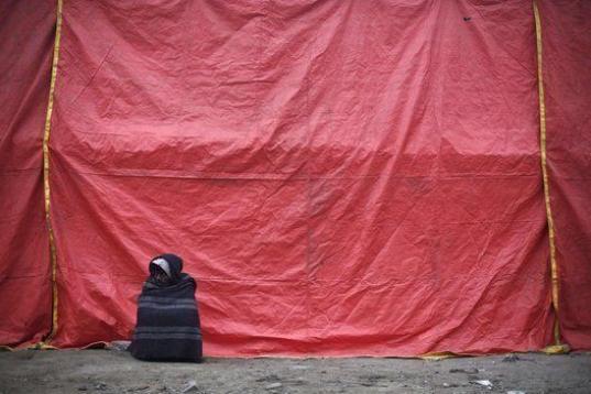 Este hombre, envuelto en una manta, descansa al lado del refugio temporal para personas sin hogar una fría mañana en Nueva Delhi (India).