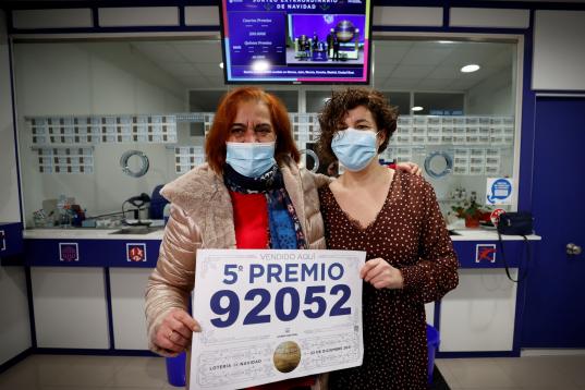 La lotera Celia Pedreira (i) y una empleada de la administración de la avenida de Oza de A Coruña, posan con el cartel del quinto premio extraído en la Lotería de Navidad, del que han vendido una serie, diez décimos, del número 92.052.