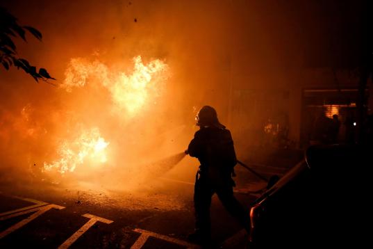 A firefighter tries to put off a fire on the street during clashes between protestors and police in Barcelona, Spain, Wednesday, Oct. 16, 2019. Spain's government said Wednesday it would do whatever it takes to stamp out violence in Catalonia, w...