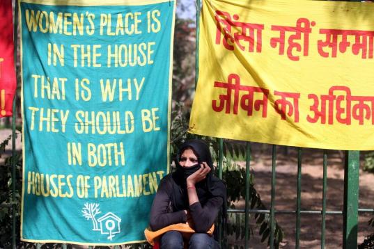 Una mujer india se sienta bajo una pancarta durante una manifestación con motivo del Día Internacional de la Mujer, en Nueva Delhi.