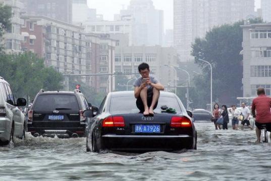 Las inundaciones en Tianjin, China, han provocado este tipo de imágenes: un hombre sentado en el techo del coche al no poder seguir avanzando. 