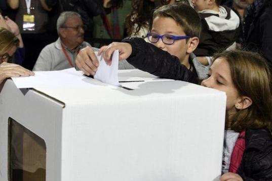 Dos niños echan el voto de su madre en la urna.