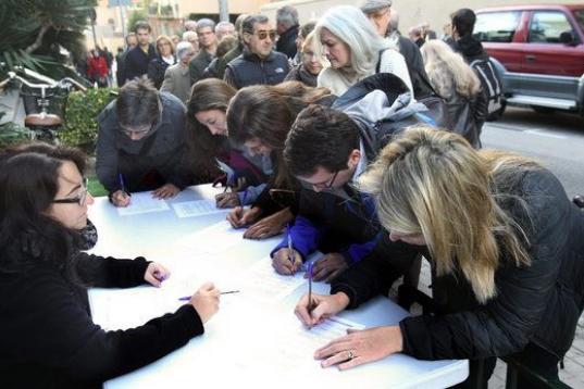 Varios ciudadanos que esperan la cola para depositar su papeleta en el colegio situado en el polideportivo la Salle de Barcelona firman el manifiesto que pide a las autoridades europeas el derecho a decidir.