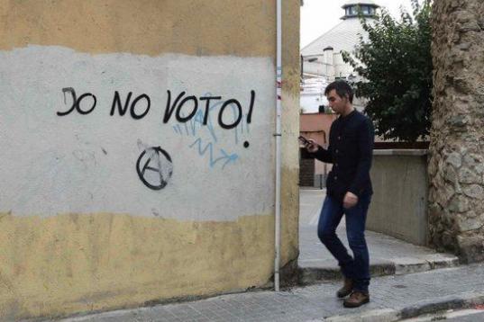 Un joven camina junto a un graffiti en el que puede leerse "Yo no voto" pintado cerca de un colegio electoral en Mataró (Barcelona).