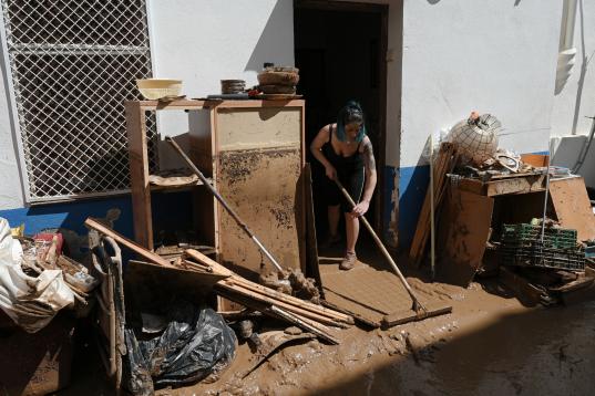 Una mujer trata de eliminar el barro de su casa, entre muebles destrozados, tras la inundación en Alcanar