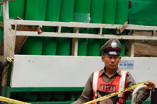 Un agente de policía tailandés vigila el área de bloqueo frente a tanques de oxígeno almacenados en un camión.