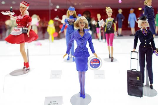 Una Barbie candidata a presidenta rodeada de una camarera, piloto de carreras, modista, azafata y piloto de aviones.
