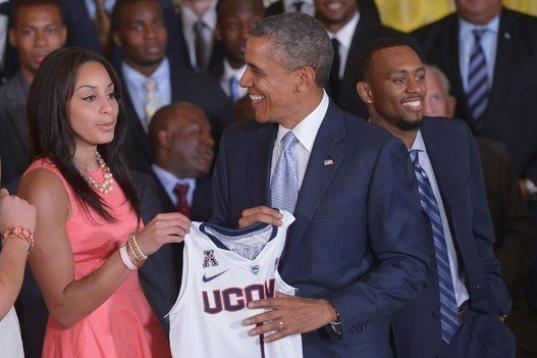 El presidente estadounidense Barack Obama sonríe después de recibir una camiseta de Bria Hartley (a la izquierda) durante un evento en honor de los NCAA 2014.