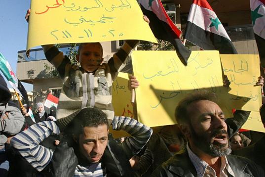 Refugiados sirios en Líbano sostienen cartulinas que dicen en árabe: "El ejército sirio libre (integrado por desertores) me protege", a la izquierda, y "Gracias al pueblo libre libanés", a la derecha, durante una manifestación frente al Com...