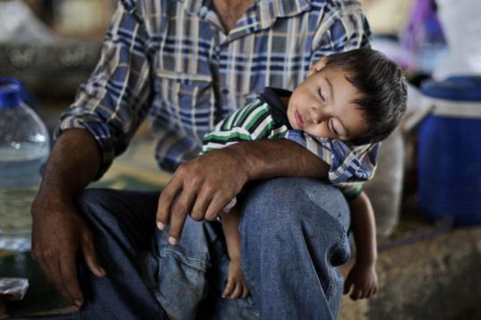 Ghassan Khalil, de 30 años, que se escapó de su pueblo Marea, Siria hace 12 días a causa del cañoneo de las tropas del gobierno a su casa, sostiene a su hijo dormido de dos años de edad. que tiene fiebre. Ellos integran un grupo de sirios q...