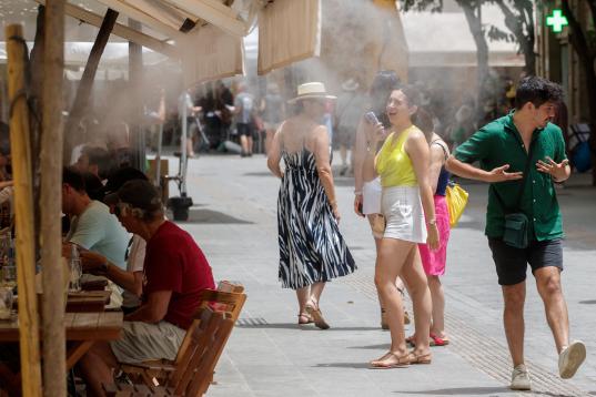 Unos turistas se refrescan con los difusores de vapor de agua de un bar de Sevilla.