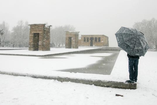Un hombre con paraguas aparece cerca del templo de Debod, un templo egipcio antiguo reconstruido en Madrid, cubierto por la fuerte nevada.