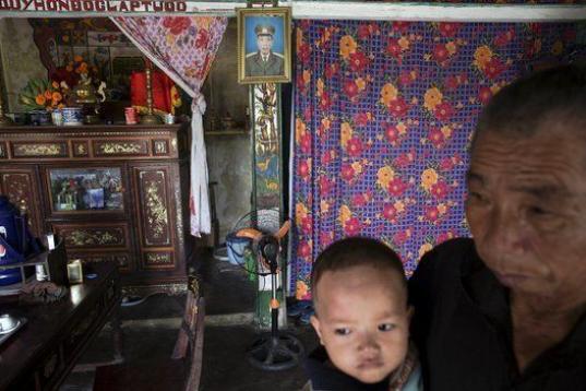 Doan Tue, con su nieta, ante una foto suya de cuando era militar. Están en su casa de Truc Ly. Doan Tue también fue soldado y tuvo hijos con discapacidad. 