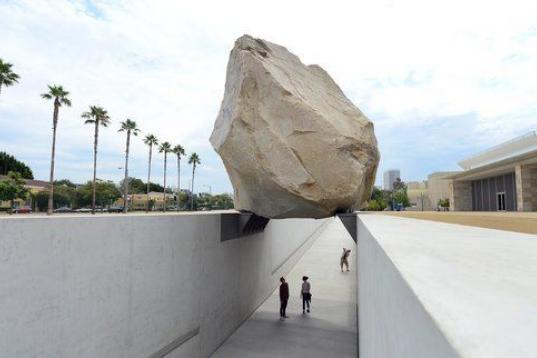 La gente camina por un sendero bajo una roca gigante expuesta en el Museo de Arte del Condado de Los Ángeles (LACMA) el 13 de julio de 2012. El bloque de granito, de 340 toneladas, forma el centro de la escultura Masa en levitación, del artist...