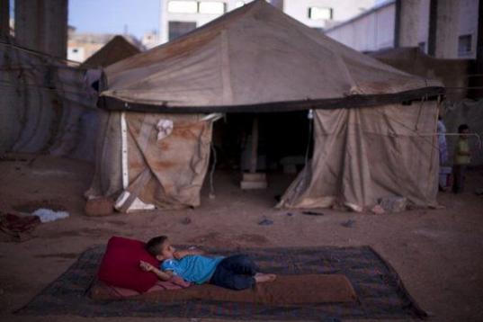 Un niño desplazado sirio se tumba en un colchón en una fábrica abandonada en Alepo, Siria. 
