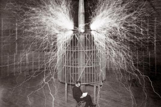 Nikola Tesla está sentado mientras hace pruebas de su invento, la Bobina de Tesla.