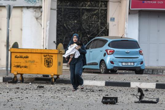 Una mujer palestina y su hija abandonan su vecindario para dirigirse a un lugar más seguro mientras los aviones de combate israelíes continúan los ataques aéreos