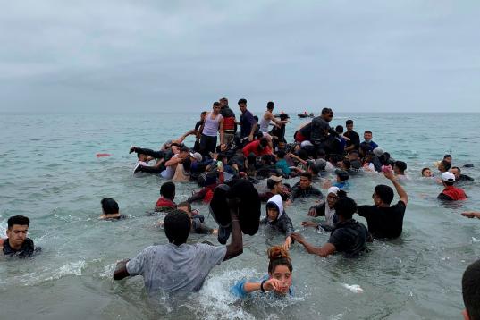 Un grupo de personas se hacen con una embarcación de las autoridades marroquíes en la playa de la localidad de Fnideq (Castillejos) para cruzar los espigones de Ceuta este martes en una avalancha de inmigrantes sin precedentes en España al re...