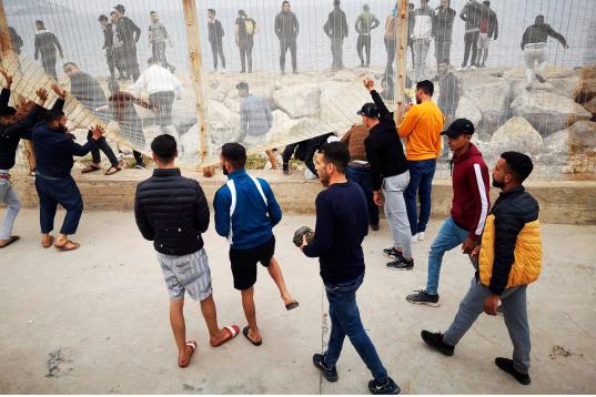 Un grupo de personas tratan de derribar la valla fronteriza en el lado marroquí mientras se dirigen este martes desde la localidad de Fnideq (Castillejos) para cruzar hacia Ceuta, en una avalancha de inmigrantes sin precedentes en España al re...