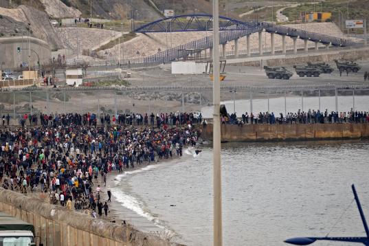 Moroccan migrants rally by a border fence in the northern town of Fnideq in an attempt to cross the border from Morocco to Spain's North African enclave of Ceuta on May 18, 2021, while Spanish troops stand to intercept them on the other side. - ...