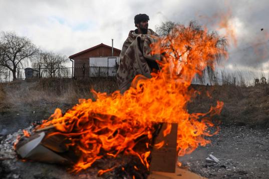 Un refugiado trata de calentarse con un fuego en la frontera ucraniano-polaca