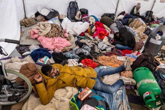 Varios refugiados se hacinan en un improvisado centro de acogida junto a sus pocas pertenencias