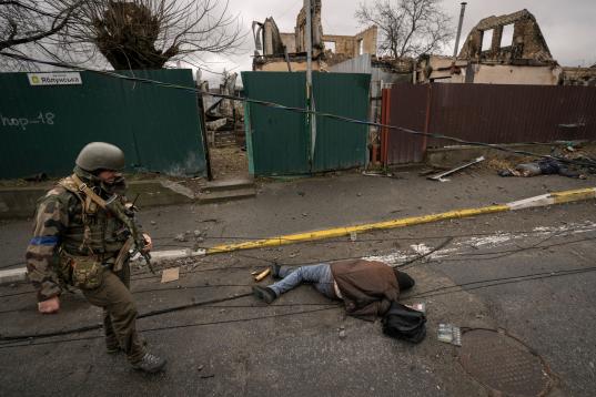 EDS NOTE: GRAPHIC CONTENT - A Ukrainian serviceman walks by lifeless bodies lying on a street in in the formerly Russian-occupied Kyiv suburb of Bucha, Ukraine, Saturday, April 2, 2022. As Russian forces pull back from Ukraine's capital region, ...