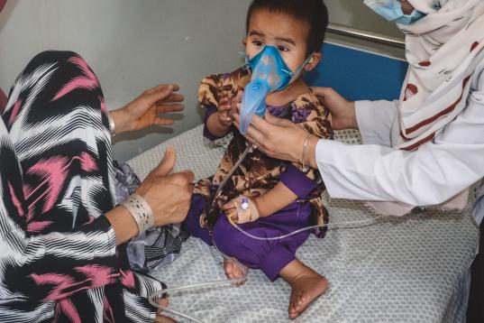Bibi Nawroz observa cómo Rihana, de dos años, recibe tratamiento con un nebulizador en la sala de sarampión apoyada por MSF en el hospital regional de Kunduz.