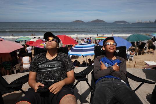 Unos niños usan gafas de sol para disfrutar del eclipse desde la playa en Mazatlán (México)
