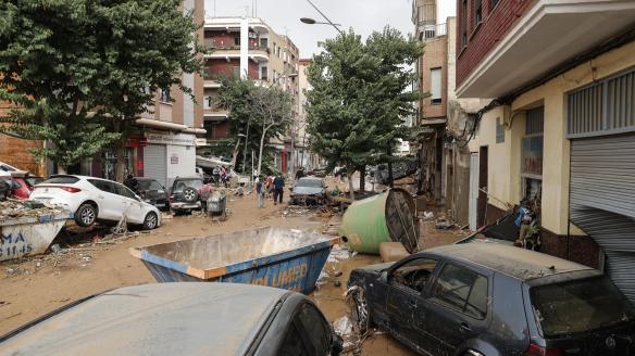 Unas personas caminan por una calle cubierta de lodo y llena de coches amontonados tras las intensas lluvias por la fuerte dana que afecta especialmente el sur y el este de la península ibérica, este miércoles en Valencia.