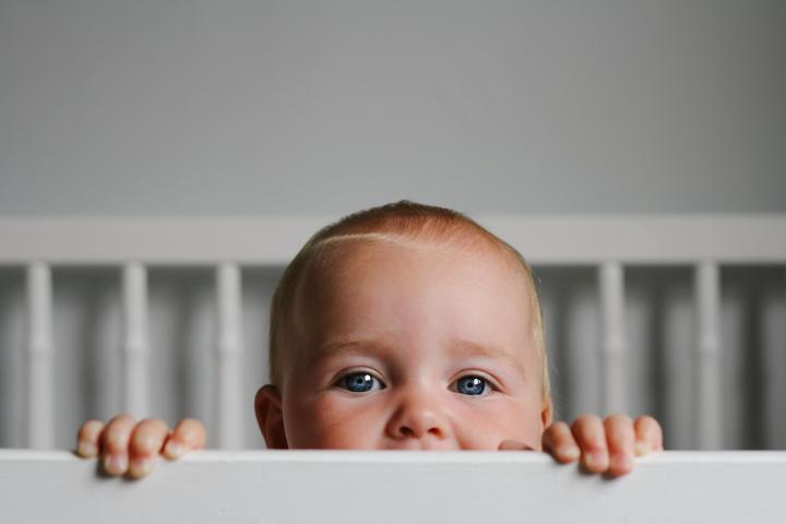 Portrait of a baby peeking over the bars of her crib.