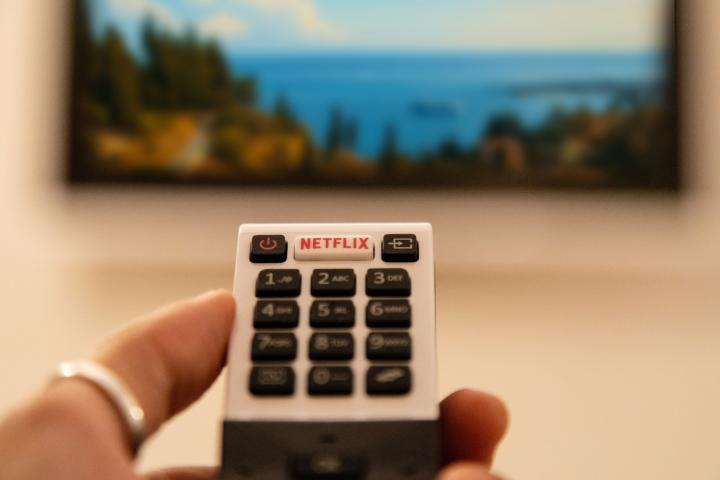 Ortigia, Italy - August 23, 2018: A hand holding television remote control with dedicated Netflix button in front of defocused smart tv