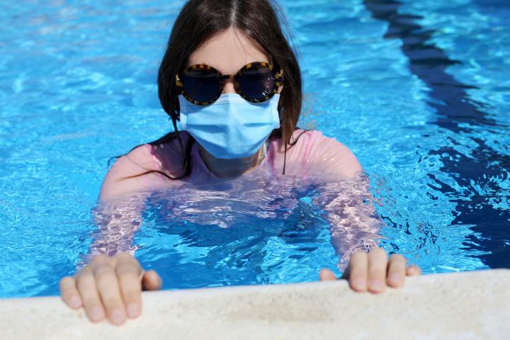 Una mujer se baña en una piscina con la mascarilla puesta.