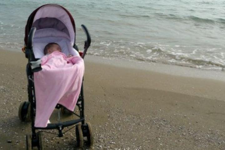 Baby girl in pram on solitary beach.