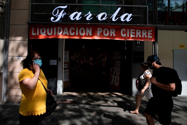 People walk past a shop that is closing down in central Barcelona on August 12, 2020. - In Spain, the coronavirus has pushed small businesses to the brink of collapse. So far, 40,000 bars, restaurants and hotels have permanently closed, with the...