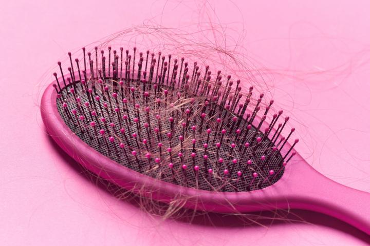Close up of a brush with loose hair in it on a pink background