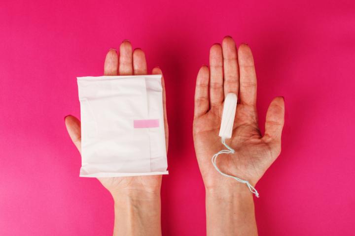 Woman holding menstrual tampon and pad on a pink background. Menstruation time. Hygiene and protection.