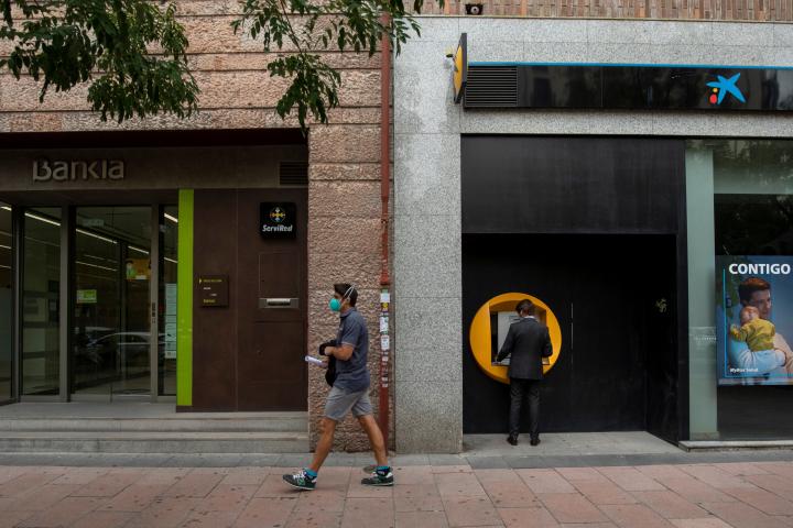 MADRID, SPAIN - SEPTEMBER 17: A man walks past branches of Bankia (L) and CaixaBank (R) on September 17, 2020 in Madrid, Spain. The Caixabank and Bankia merger will create Spain's biggest lender, with a market value of about 16bn euros and hold ...