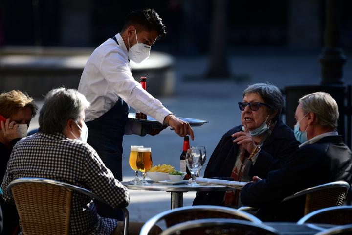 A waiter serves customers at a restaurant in Barcelona on November 23, 2020 as bars, restaurants and movie theatres were allowed to reopen in Spain's northeastern region of Catalonia after being closed for over a month as part of measures to slo...