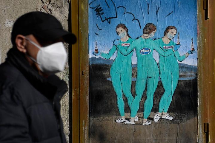 Un hombre con mascarilla pasa por delante de un grafiti del artista italiano TvBoy en Barcelona, titulado 'Las tres vacunas' en referencia a 'Las tres Gracias' de Rafael.