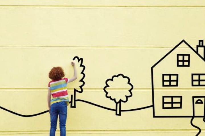 Girl drawing a house and trees onto a wall