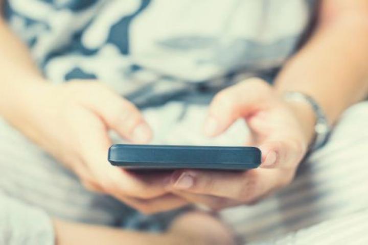 A woman sitting on her legs on the couch at home interacts with her mobile phone