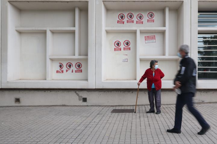 Dos personas mayores en el centro de salud de Pavones (Madrid), donde varios carteles dicen 'Urgencias Cerradas, tu salud vendida', el 21 de octubre de 2022.