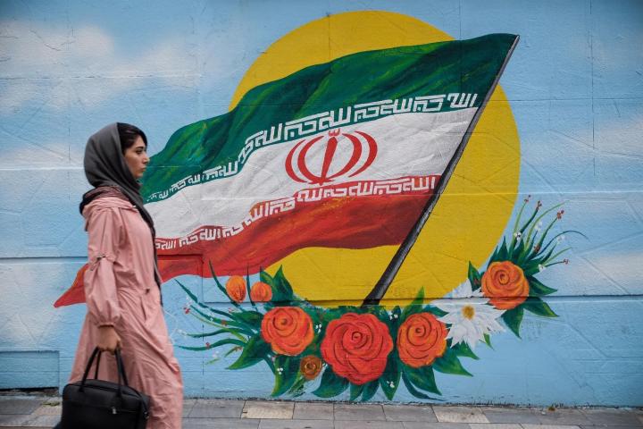 Una mujer camina frente a un mural con la bandera de Irán situado en una de las calles de Teherán