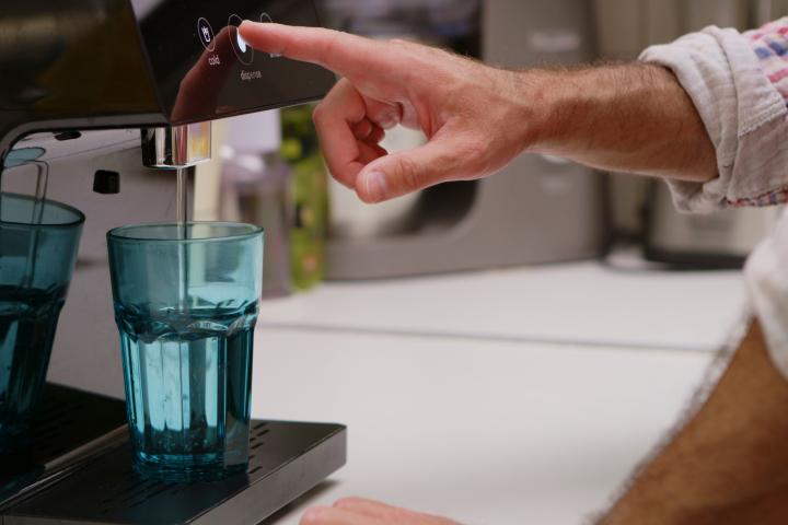 Un hombre se sirve un baso de agua en un dispensador instalado en su casa