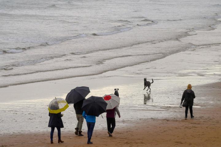 Unas personas pasean con paraguas en una playa en Gijón este sábado.