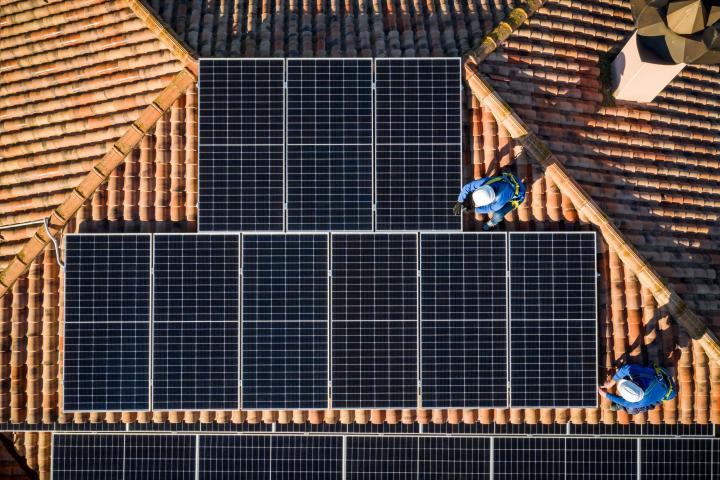 Imagen de archivo de dos operarios instalando un sistema de placas solares en el teja de una vivienda española.